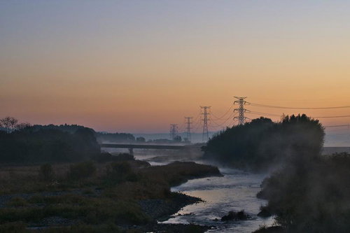 河川沿いの自然に囲まれた送電線鉄塔群の夜明けの風景