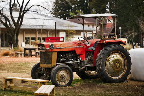 古い農場跡地に放置された赤いトラクターと木製のベンチ
