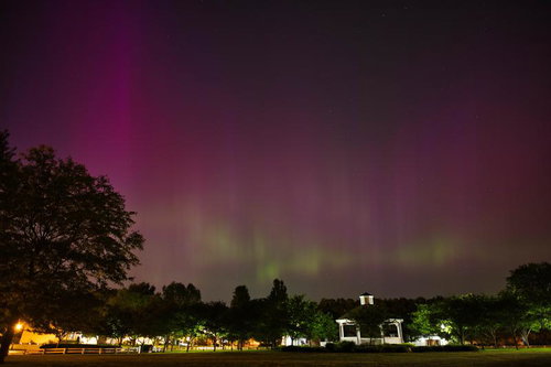 公園のガゼボを照らすピンク色のオーロラと星空