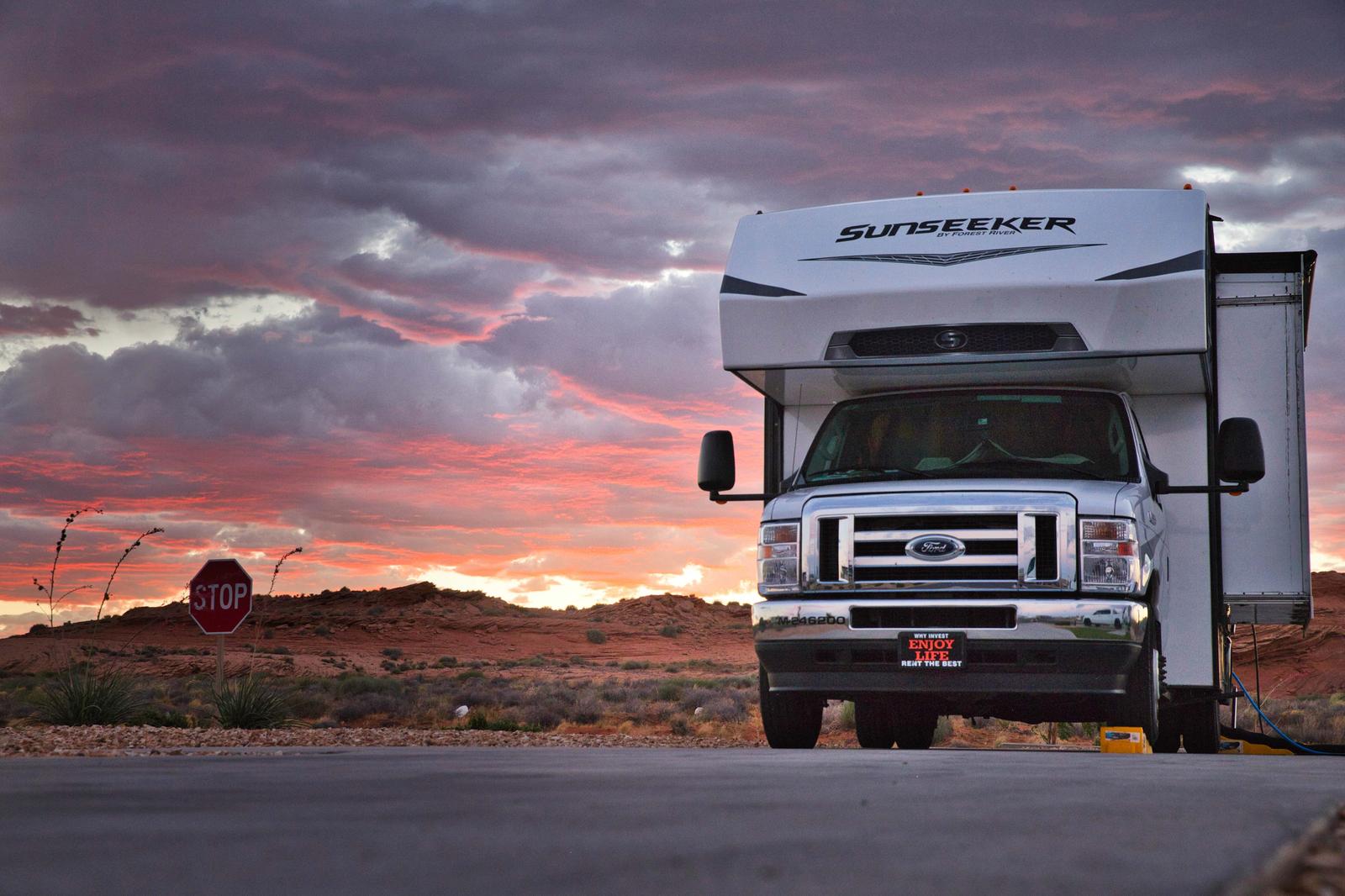 夕焼け空の下、砂漠に停車する白いキャンピングカー