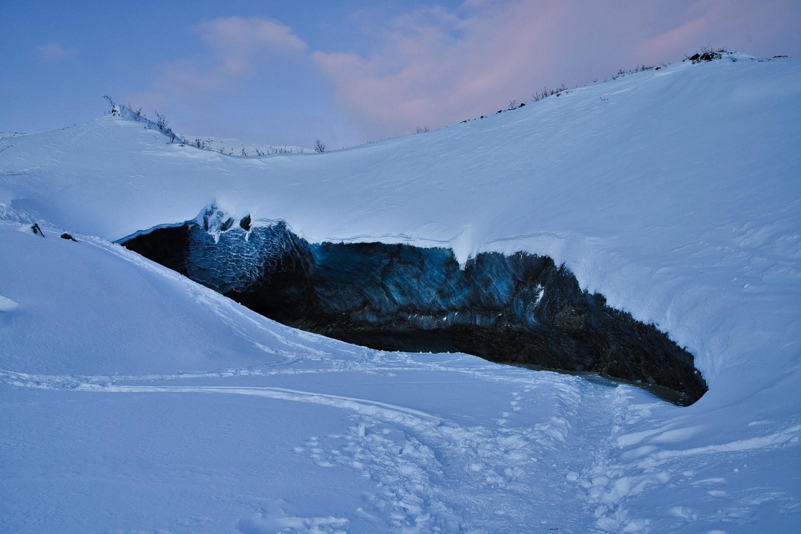 雪に覆われた山肌から突き出す黒い岩盤の氷の洞窟