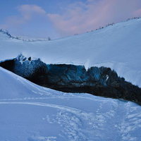 雪原に突き出す黒い氷の洞窟と探検者の足跡の写真