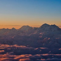 オレンジ色に染まる夕暮れのデナリの雪山と雲海の写真