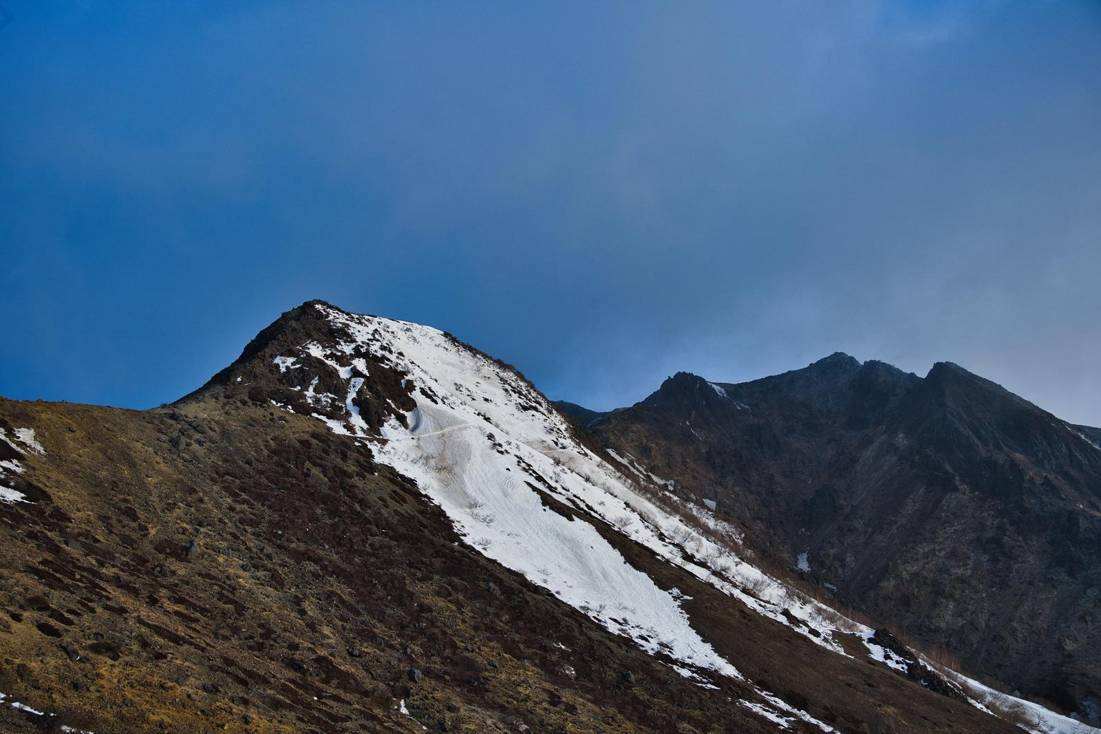 雪解けが進む山の斜面と稜線、青空に雲が広がる春山の風景