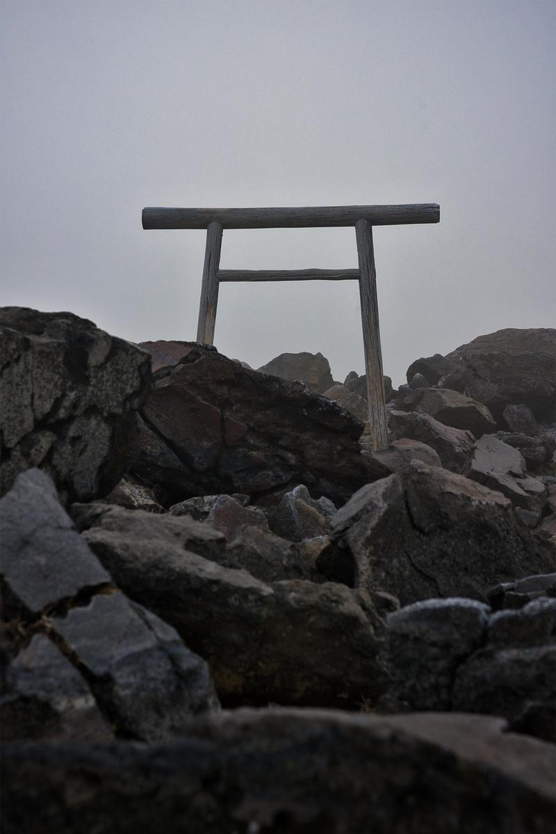 An old wooden torii gate (torii) standing at the rocky summit with a misty, cloudy sky