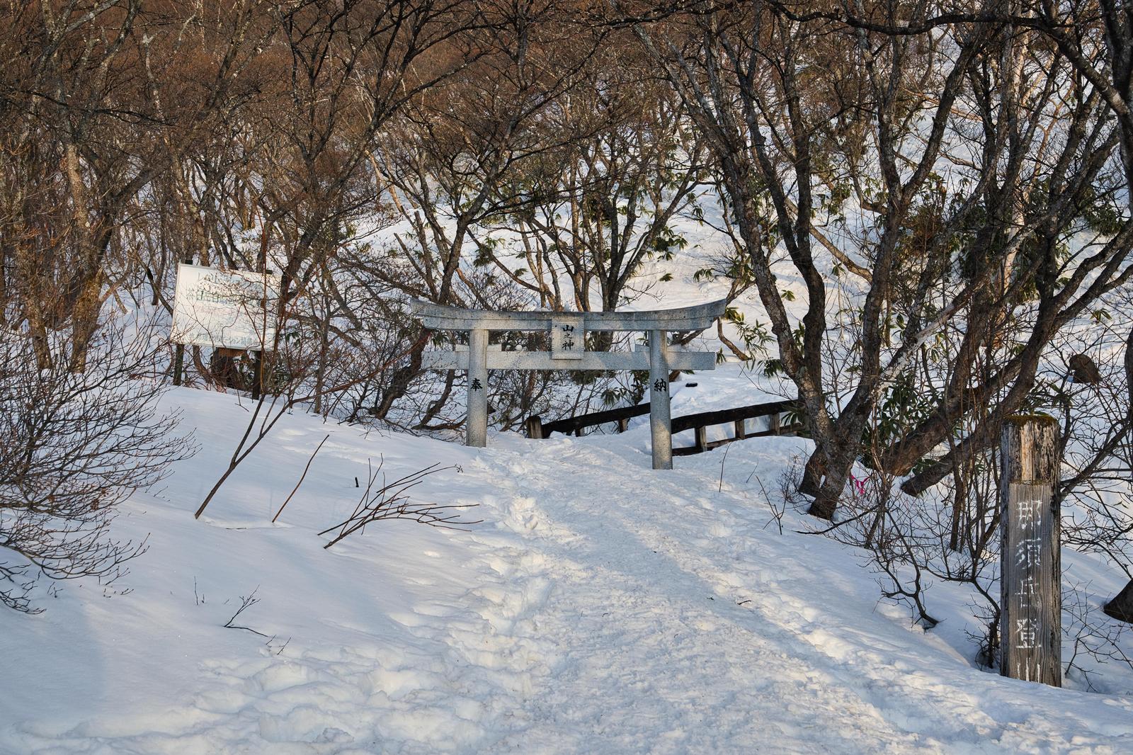 那須岳の登山道入口に立つ石鳥居と雪に覆われた雑木林