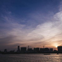 海を隔てて見える夕焼けに染まる都市ビル群のシルエットの写真