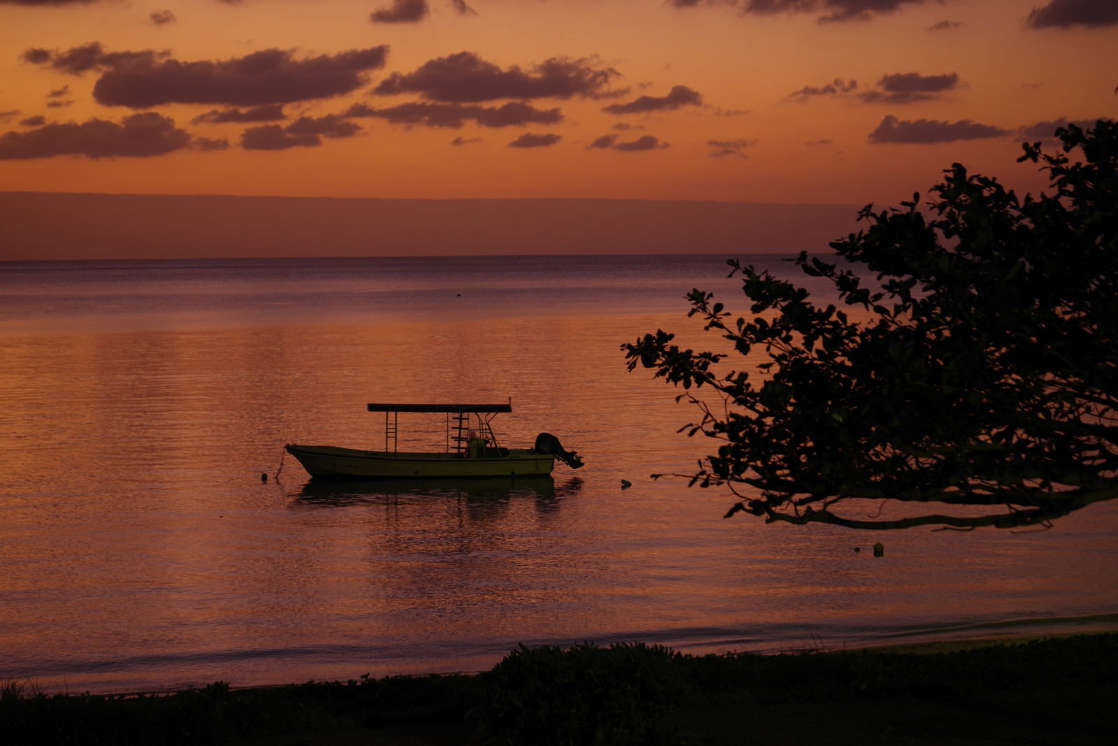 夕焼けで染まった海に浮かぶ一艘のボートと沖縄の夕景