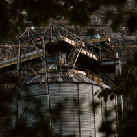 茂みの向こうに見える古い工場と採石場の廃墟の写真