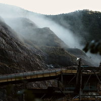 霧に包まれた山間の工場から立ち上る白い蒸気の写真