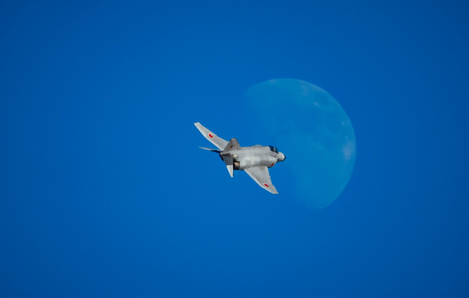 青空に浮かぶ大きな月に向かって飛行するF-4ファントム戦闘機