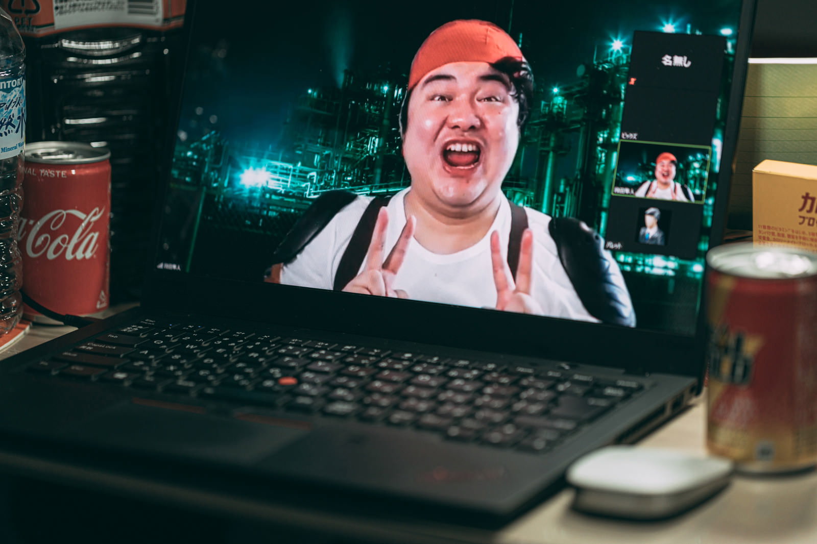 ノートパソコンのビデオチャット画面に映る、赤いヘアバンドをかぶった男性がダブルピースで笑顔を見せている［モデル：段田隼人］
