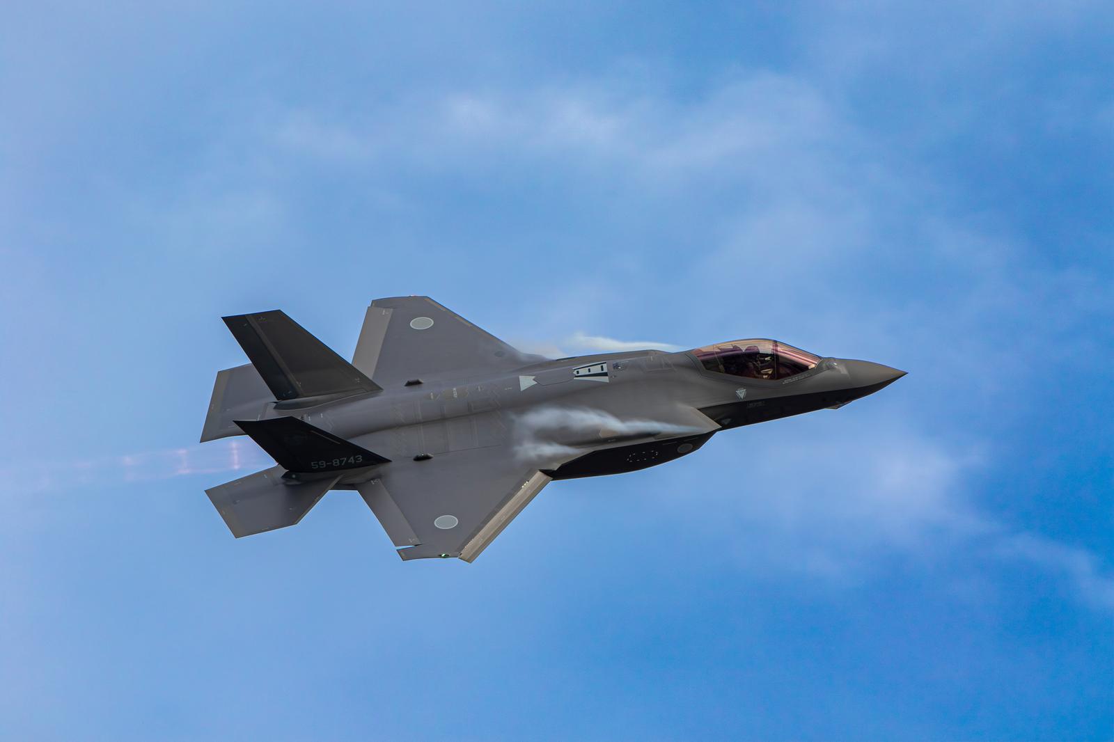 青空と雲を背景に飛行するグレーのF-35ステルス戦闘機