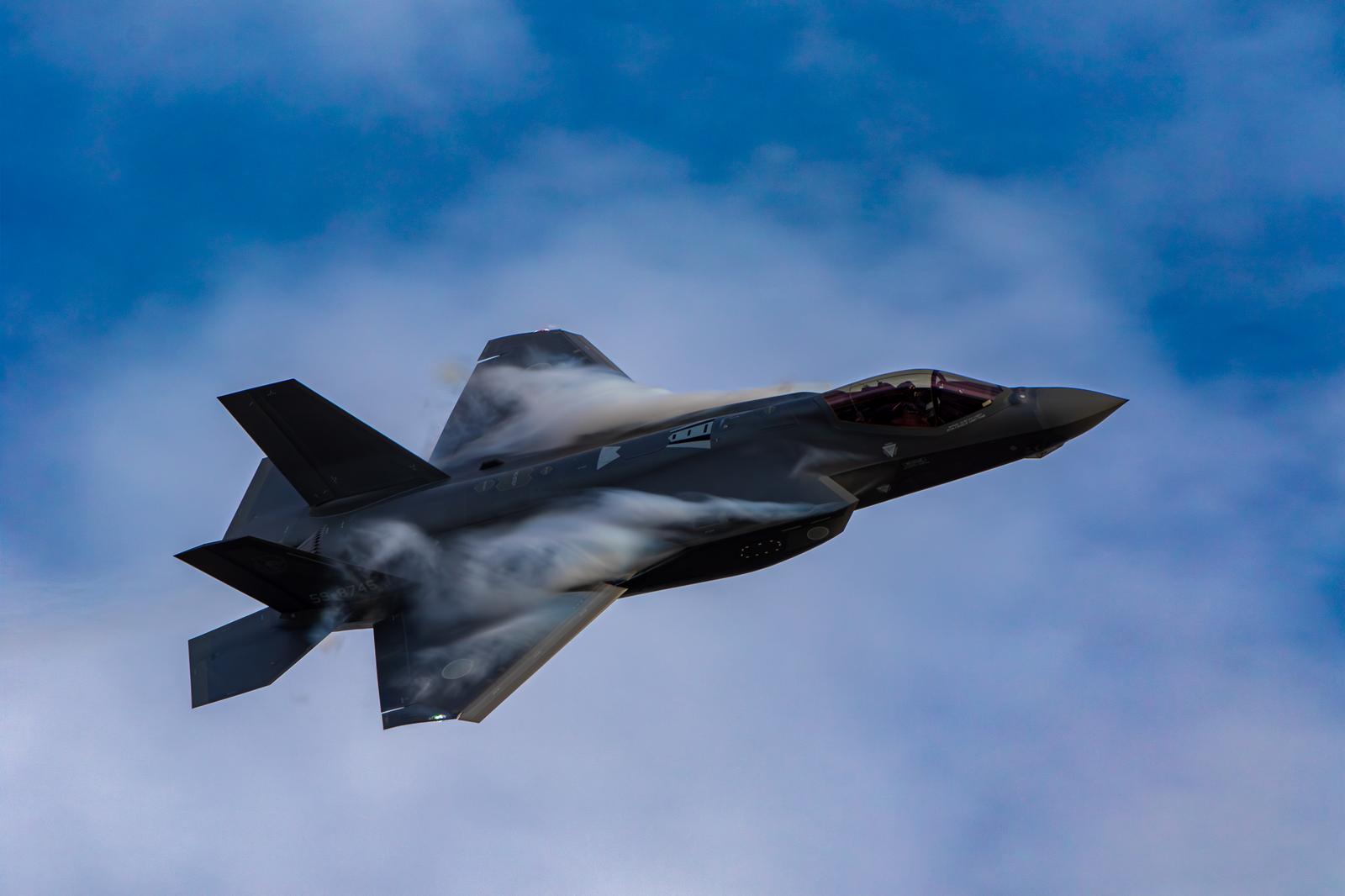 青空と雲の間を高速飛行する航空自衛隊のステルス戦闘機F-35