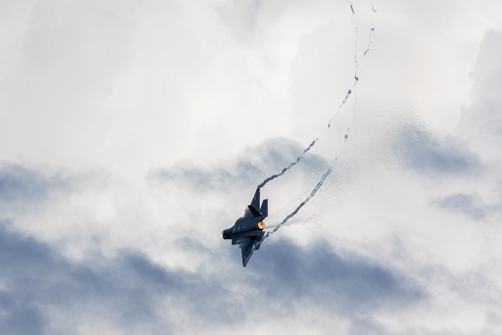 Japan Air Self-Defense Force (JASDF) fighter jet climbing through clouds while trailing a contrail