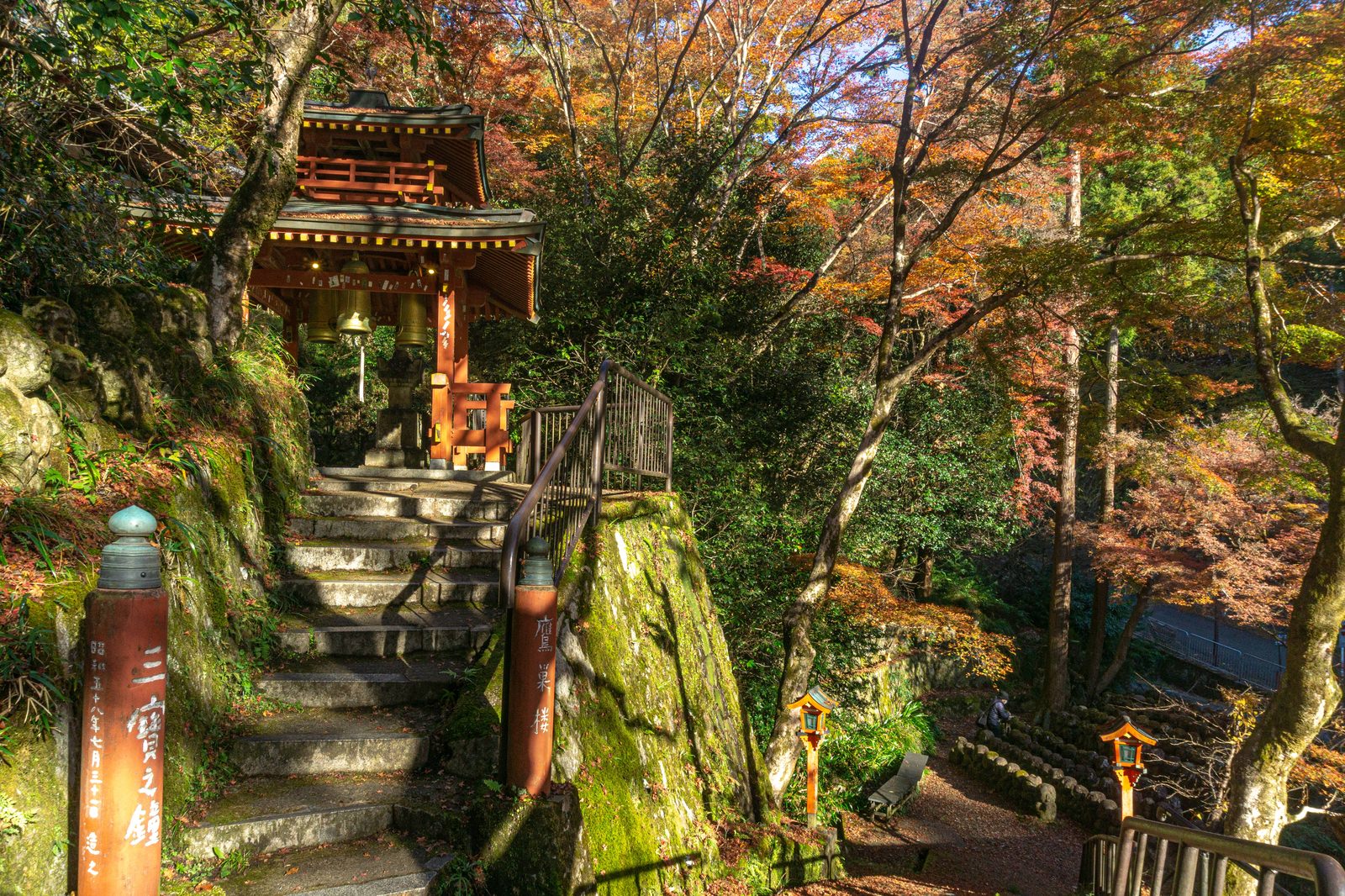 愛宕念仏寺の鐘楼に金色の鐘が3つ吊り下げられ、周囲に紅葉した木々が見える