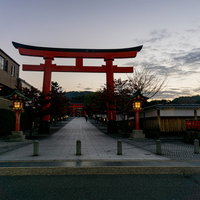 足元からのライトに照らされた早朝の伏見稲荷大社社号標と一番鳥居から伸びる灯りが残る石畳の写真