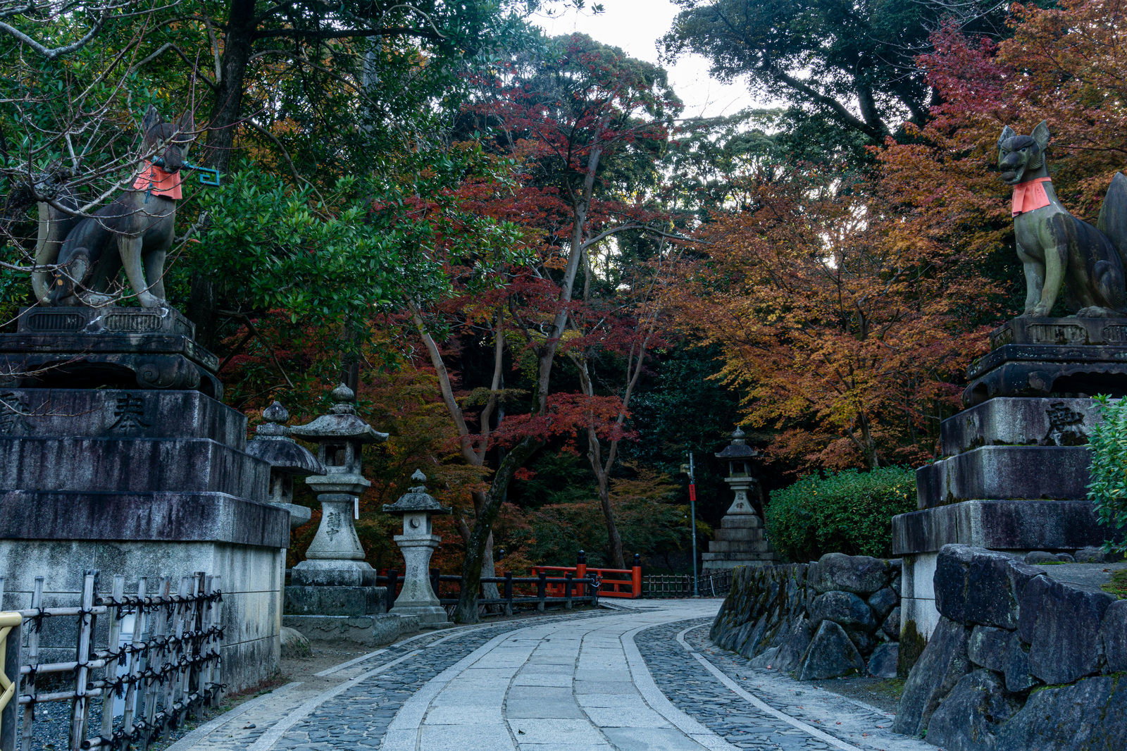 伏見稲荷大社の石畳参道に立つ狛狐と色づいた紅葉の風景