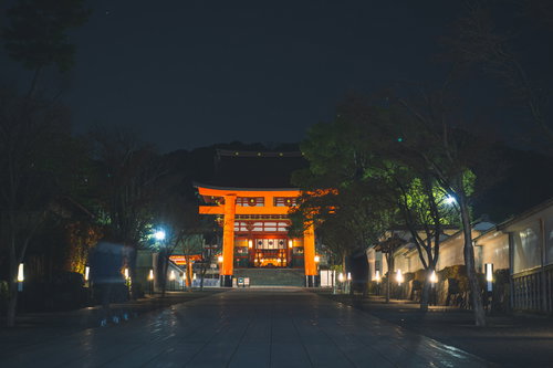 灯篭の光がうっすらと反射する石畳の先に浮かび上がる伏見稲荷大社の二番鳥居