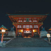 夜間ライトアップされた朱塗りの伏見稲荷大社楼門と石段の写真