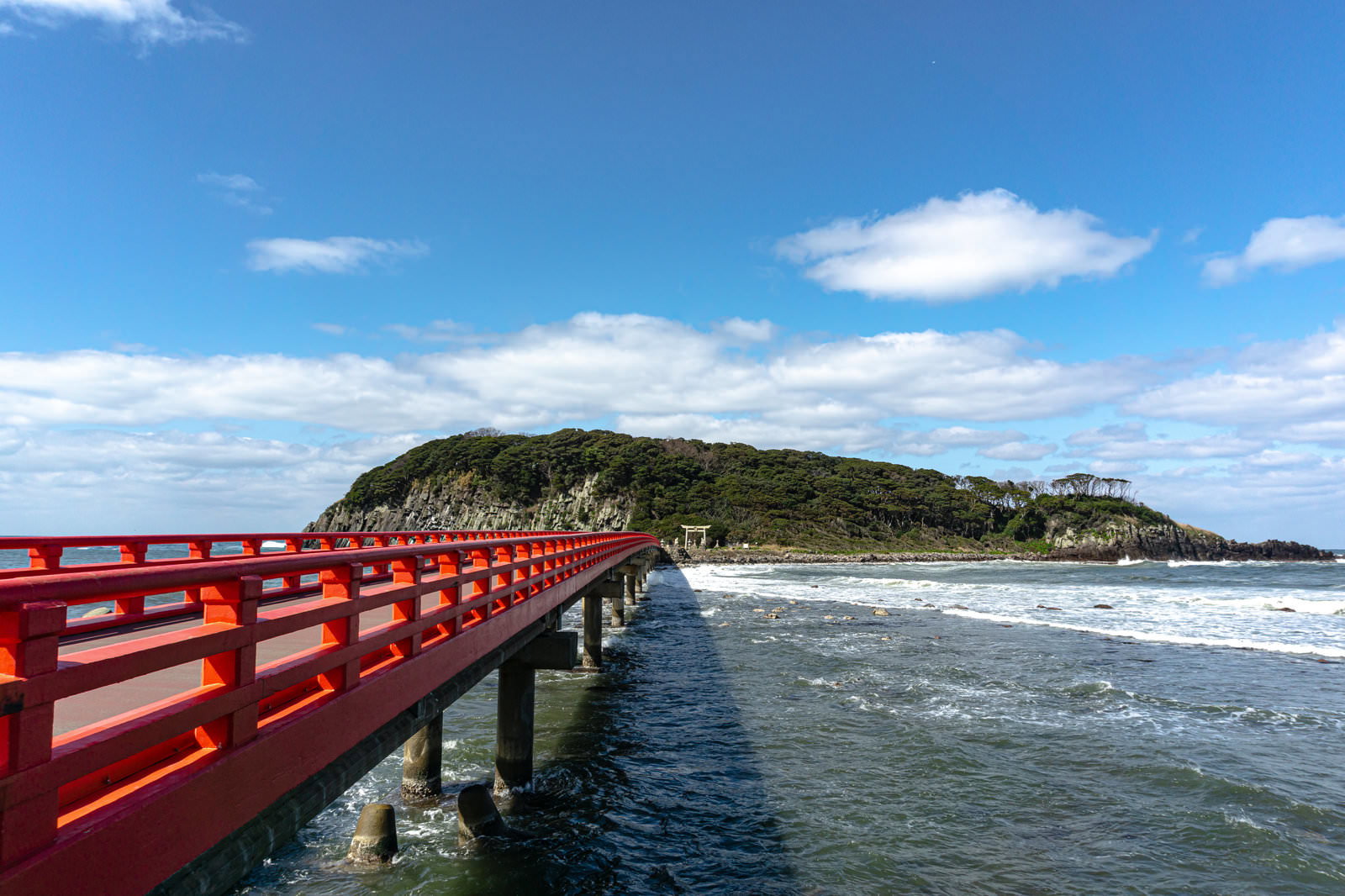 朱色の橋の先に見える海の神様の島として崇められる雄島と寄せる波