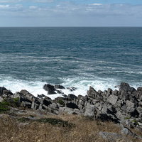 打ち付けた波が白く泡立つ島西側岩場の波打ち際の写真