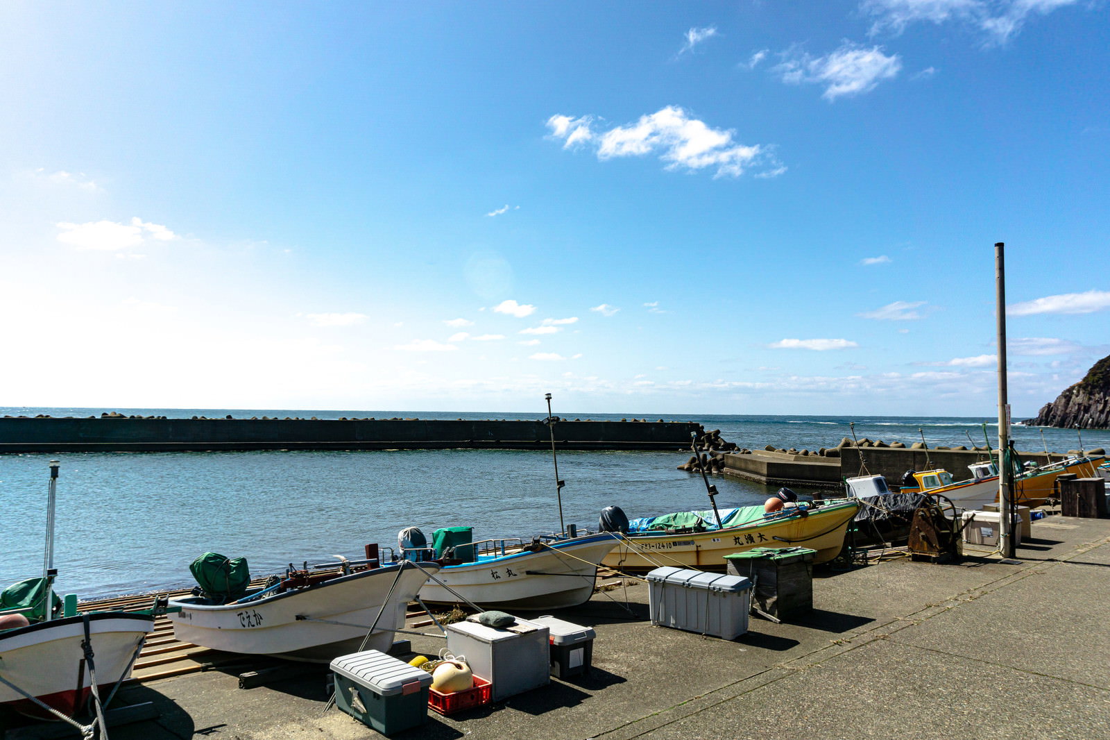 福井県の安島漁港に係留された複数の漁船と堤防、背景に雄島が見える風景