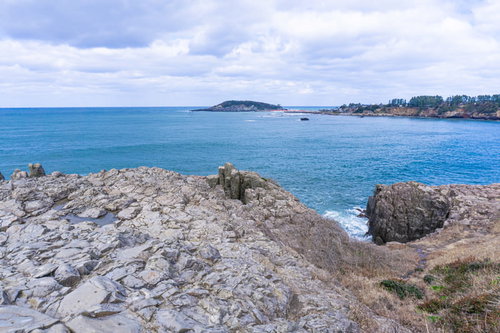 雄島とそこにかかる赤い橋を東尋坊のゴツゴツとした岩場から望む