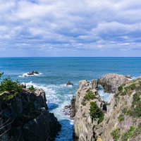 切り立った岩壁の間に打ち寄せ白く泡立つ波の写真