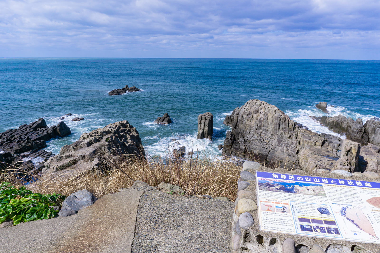 東尋坊の遊歩道から見た千畳敷の岩場と海の風景、手前に説明パネル