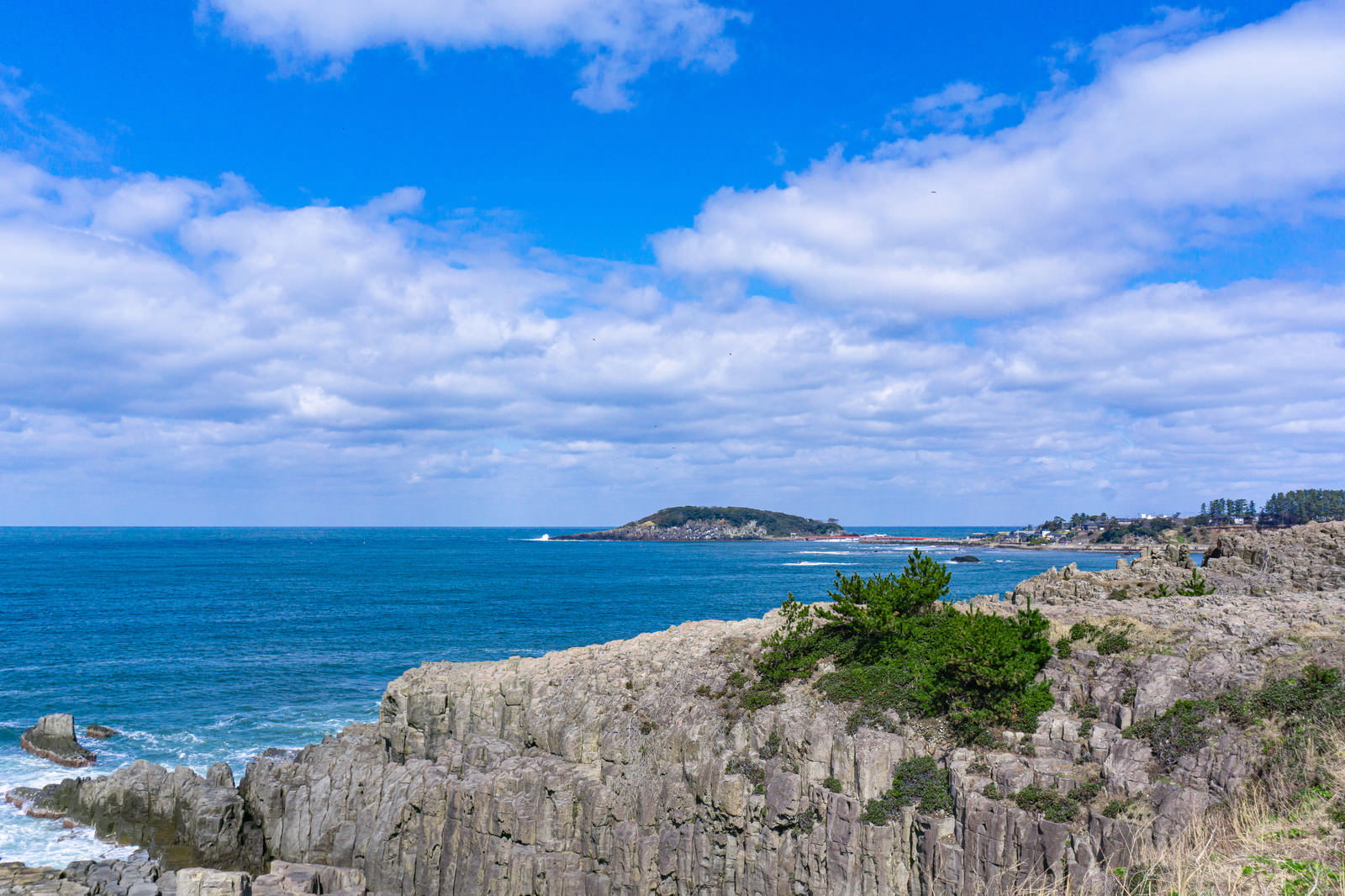 東尋坊の断崖絶壁と青い海、遠方に雄島が見える福井県の景色