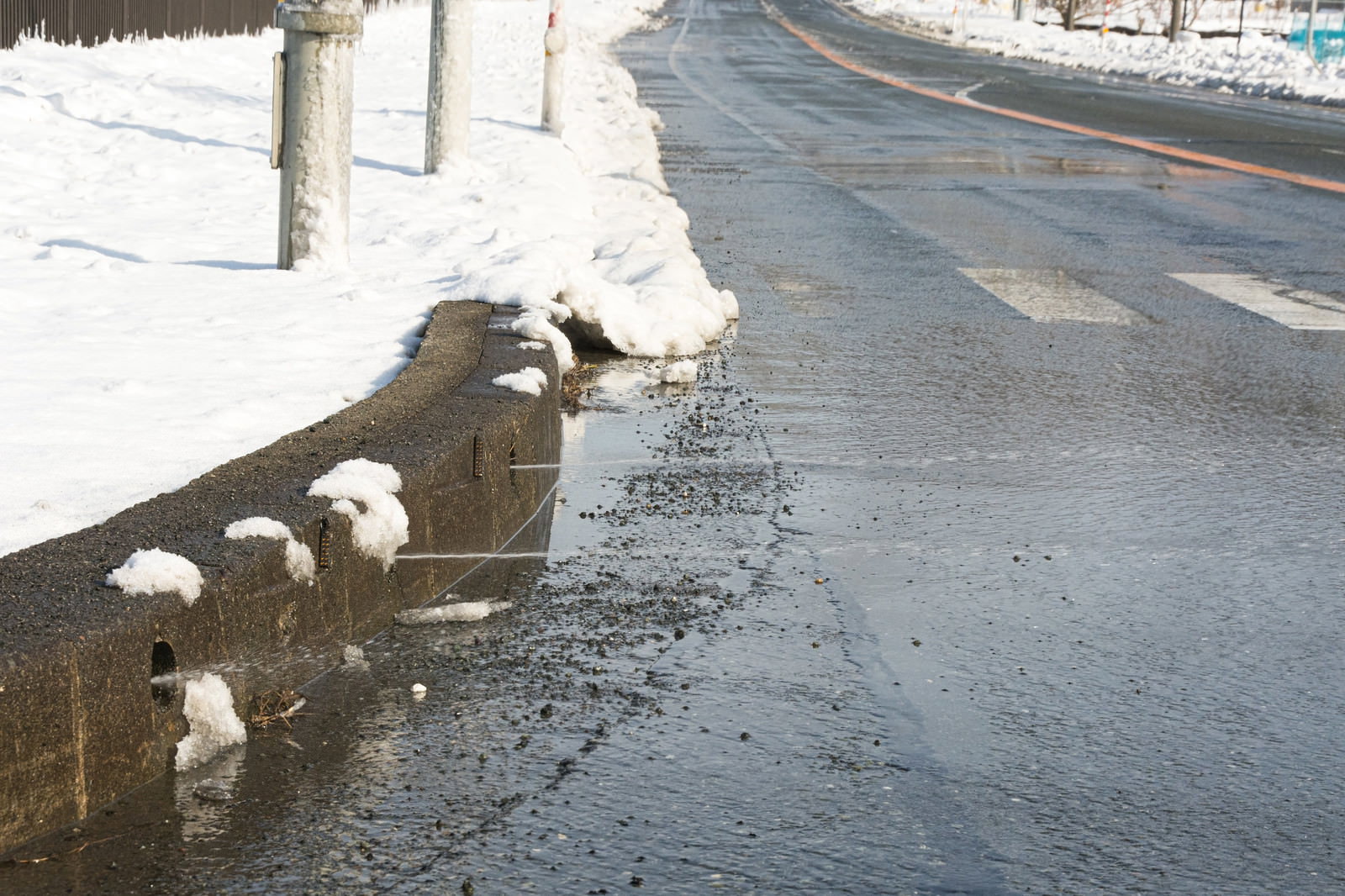 道路脇の縁石から融雪水が勢いよく噴き出している冬の光景