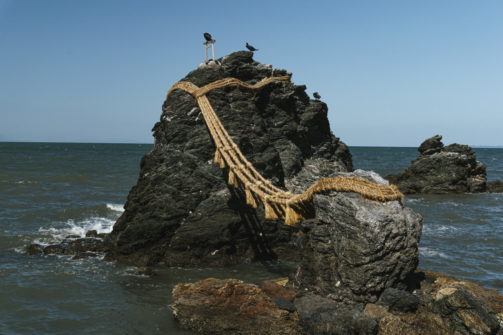 注連縄で結ばれた夫婦岩と奥に見えるカエルの形をした奇岩