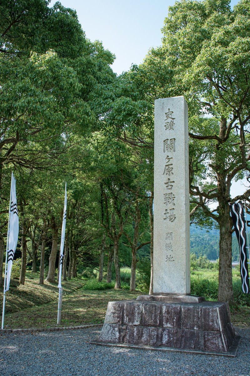 緑豊かな木々を背景に白い石碑が立っている開戦地の風景