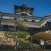 天守閣の地下二階にあたる石垣に作られた出入口にあるテントと、青空に堂々とそびえる天守閣の写真