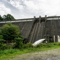 ダム下流の空き地から見るどんよりした空を背景に建つ重力式コンクリート型式の黒田ダムの写真