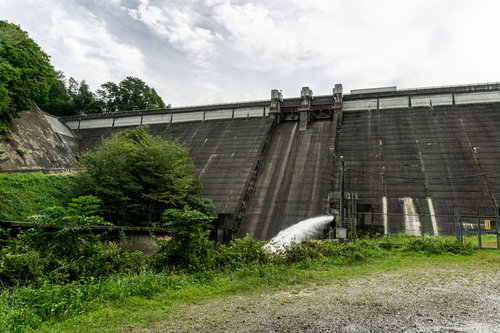 ダム下流の空き地から見るどんよりした空を背景に建つ重力式コンクリート型式の黒田ダム