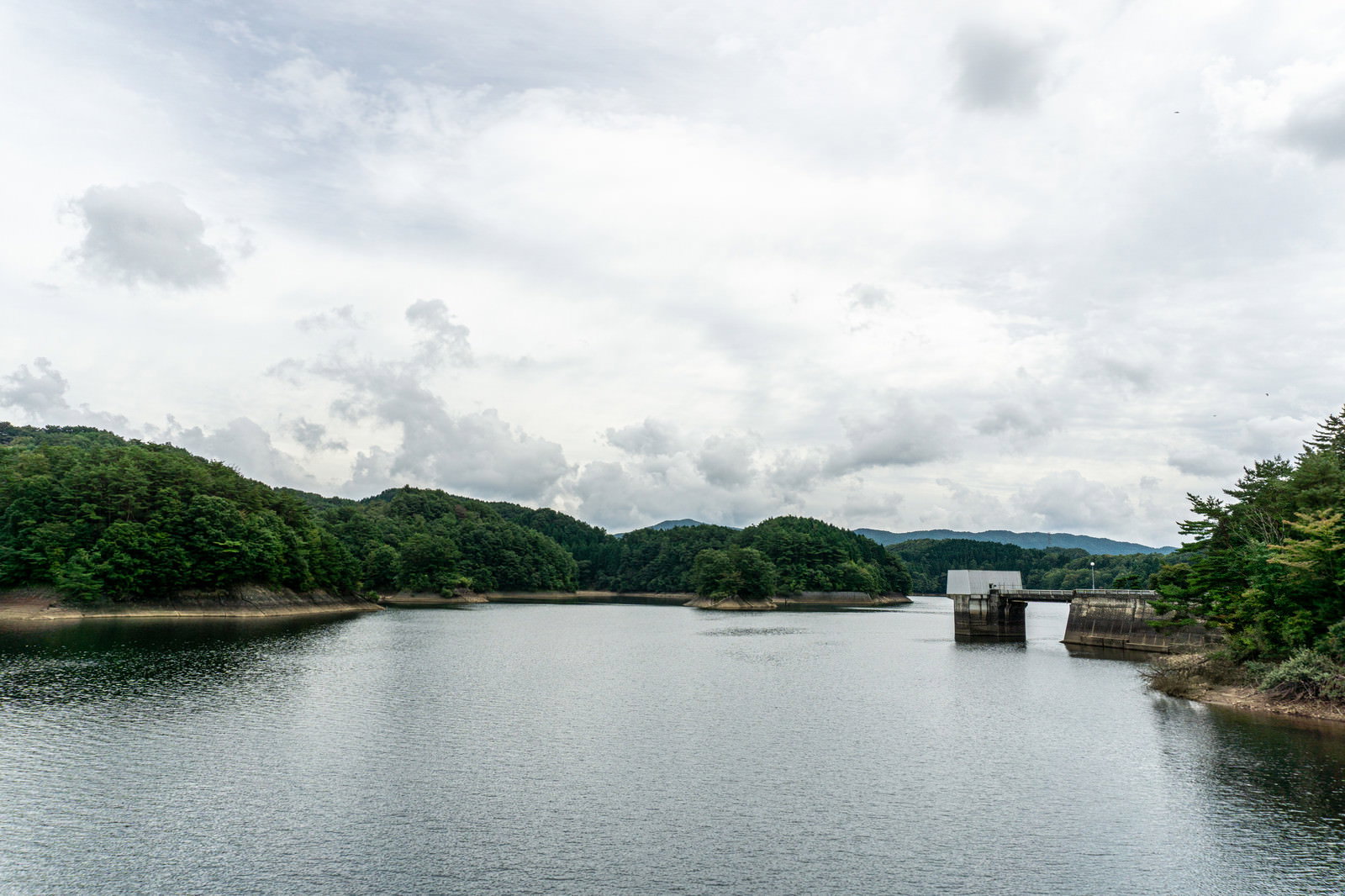 厚い雲に覆われた空の下に静かに広がる黒田湖の風景