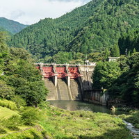 周囲の山の緑に囲まれた中で赤いゲートが一際美しく目立つ矢作第二ダムの写真