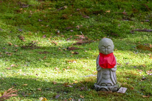 落ち葉が散らばる苔の上の石仏