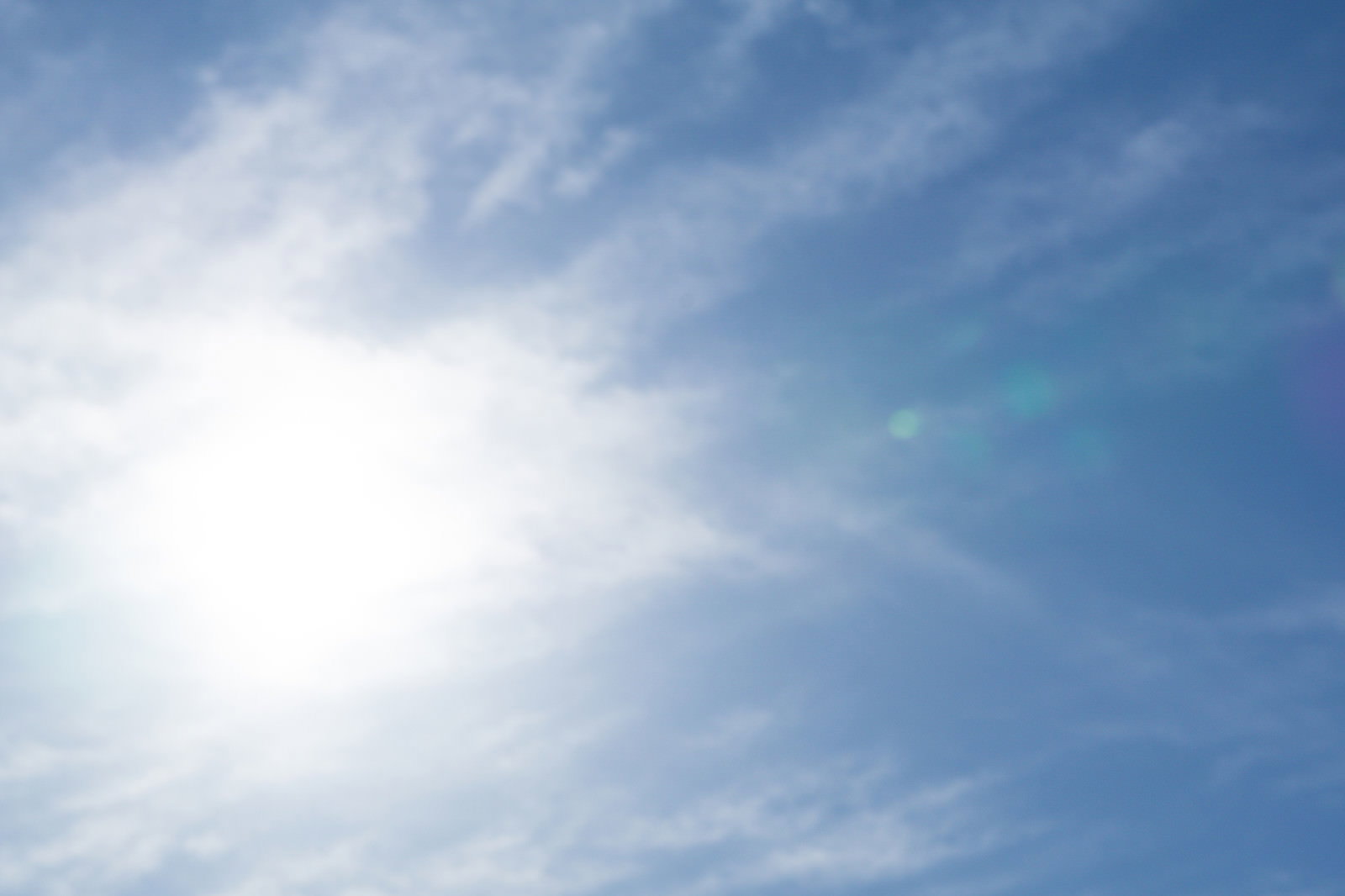 青空に薄い白い雲が広がり、太陽の光が雲を透して見える自然の風景