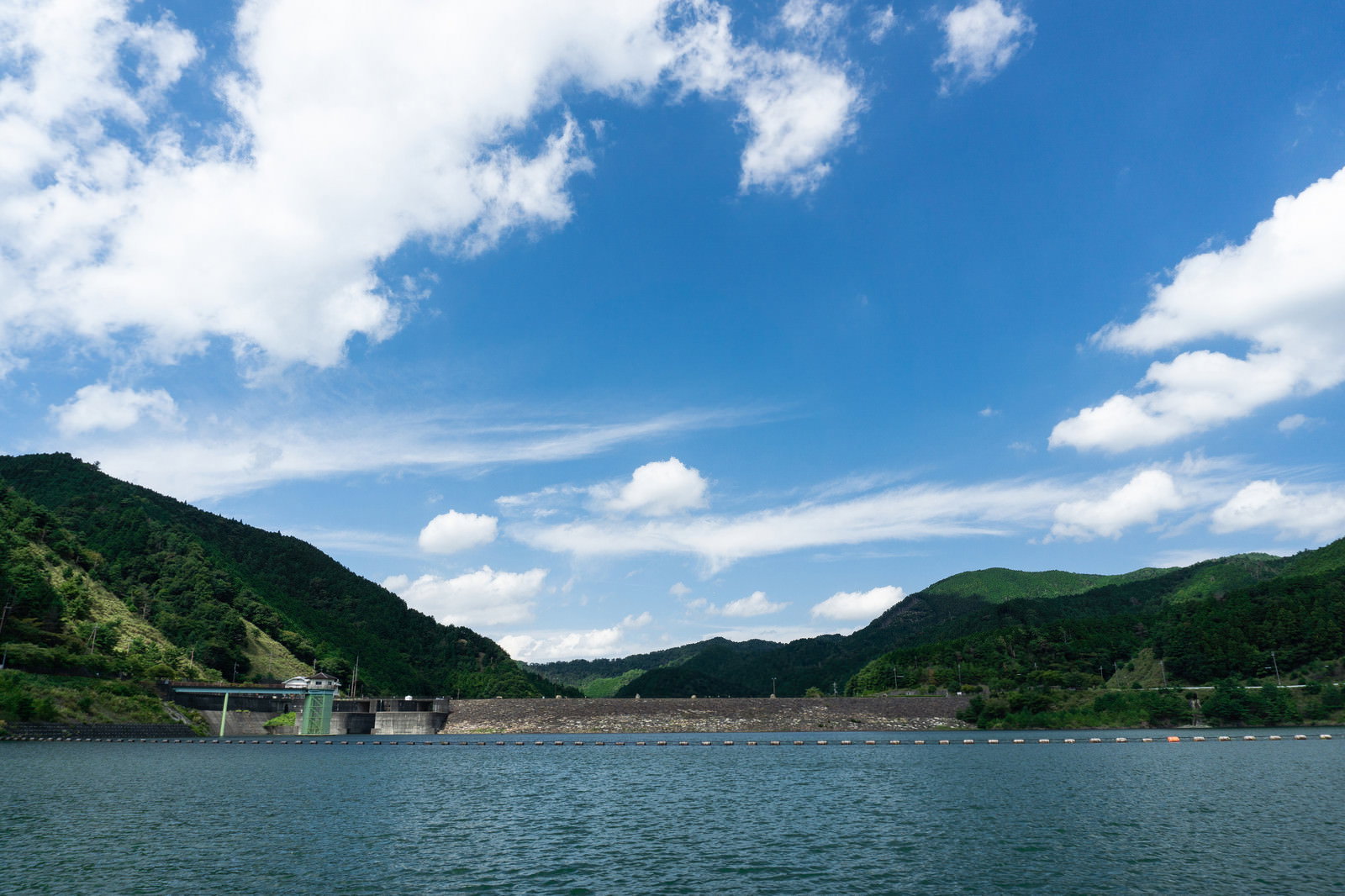 青空の下で緑の山々に囲まれた青土ダムの湖面を遊覧ボート場から撮影した風景