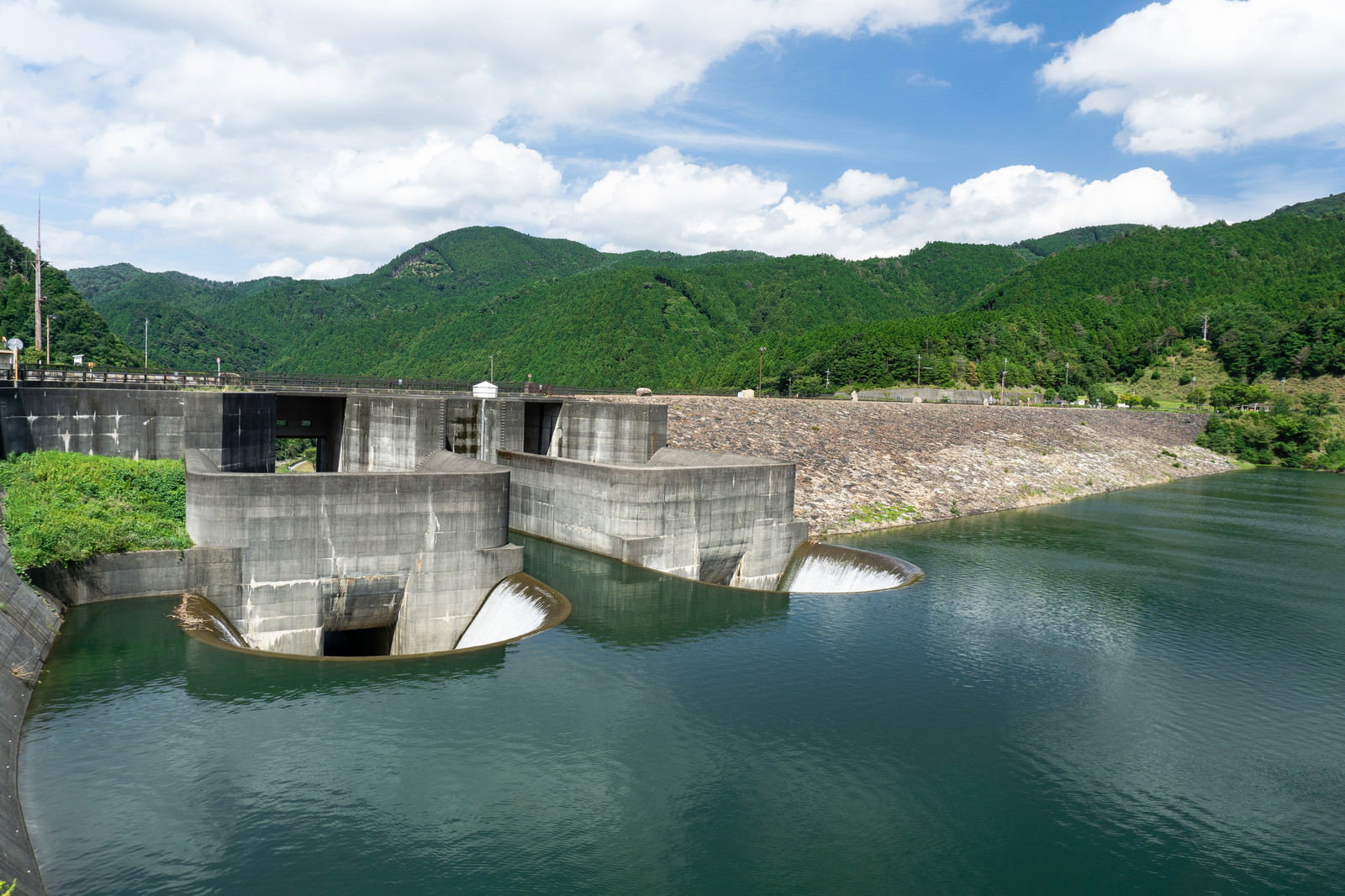 青土ダムの洪水吐と緑の山々に囲まれたダム湖の風景
