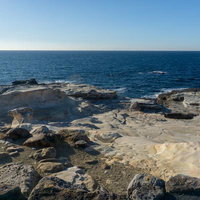 千畳敷の平らな岩盤と紺碧の海が広がる海岸線の写真