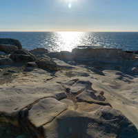 太陽光が反射する千畳敷の岩場と青い海の写真