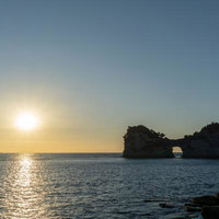 白浜の円月島に沈む夕日とオレンジに染まる海面の写真