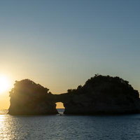 夕日に照らされる円月島と海面に輝く光の道のシルエットの写真