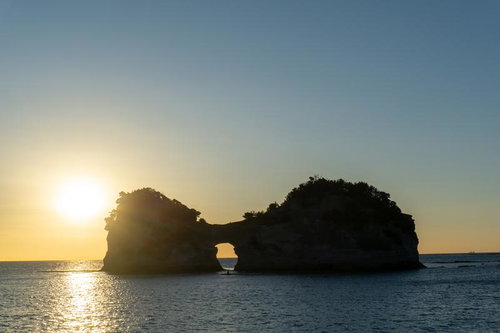 夕日に照らされる円月島と海面に輝く光の道のシルエット