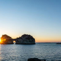 円月島の海に沈みゆく夕陽とオレンジ色の空を見守るグラスボートの写真