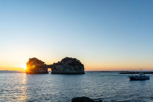 円月島の海に沈みゆく夕陽とオレンジ色の空を見守るグラスボート